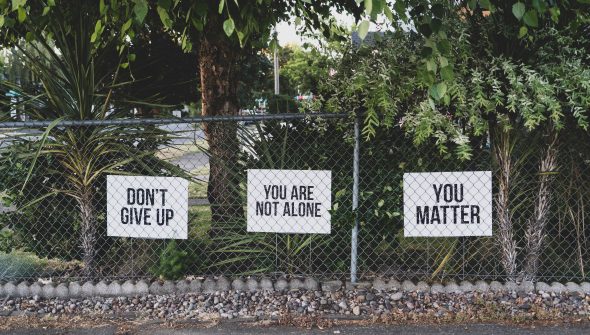 three signs on a fence saying, "don't give up," "you are not alone" and "you matter"