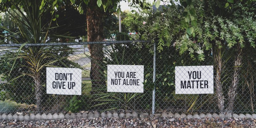 three signs on a fence saying, "don't give up," "you are not alone" and "you matter"